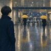 駅の改札外コンコースで同じ黄色い傘を持つ人たちを見つめる人物のイラスト